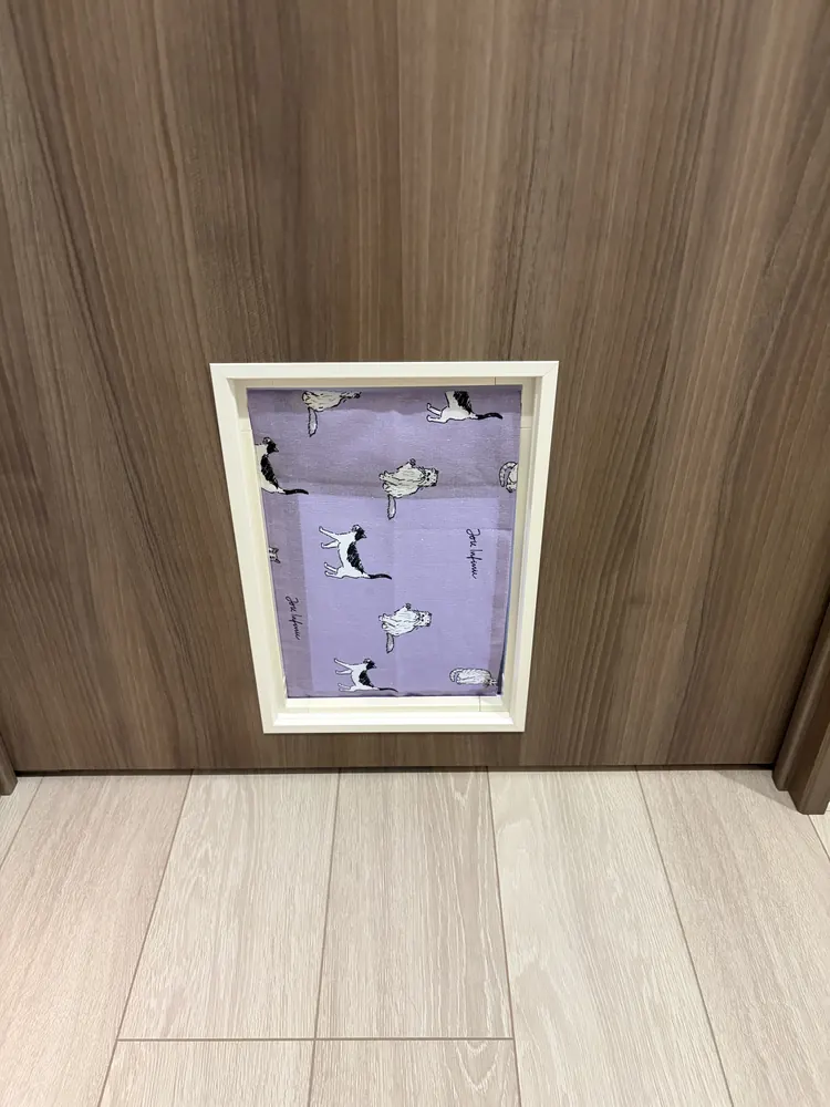 壁に取り付けられた完成品。白い枠に猫柄の布が掛かっている